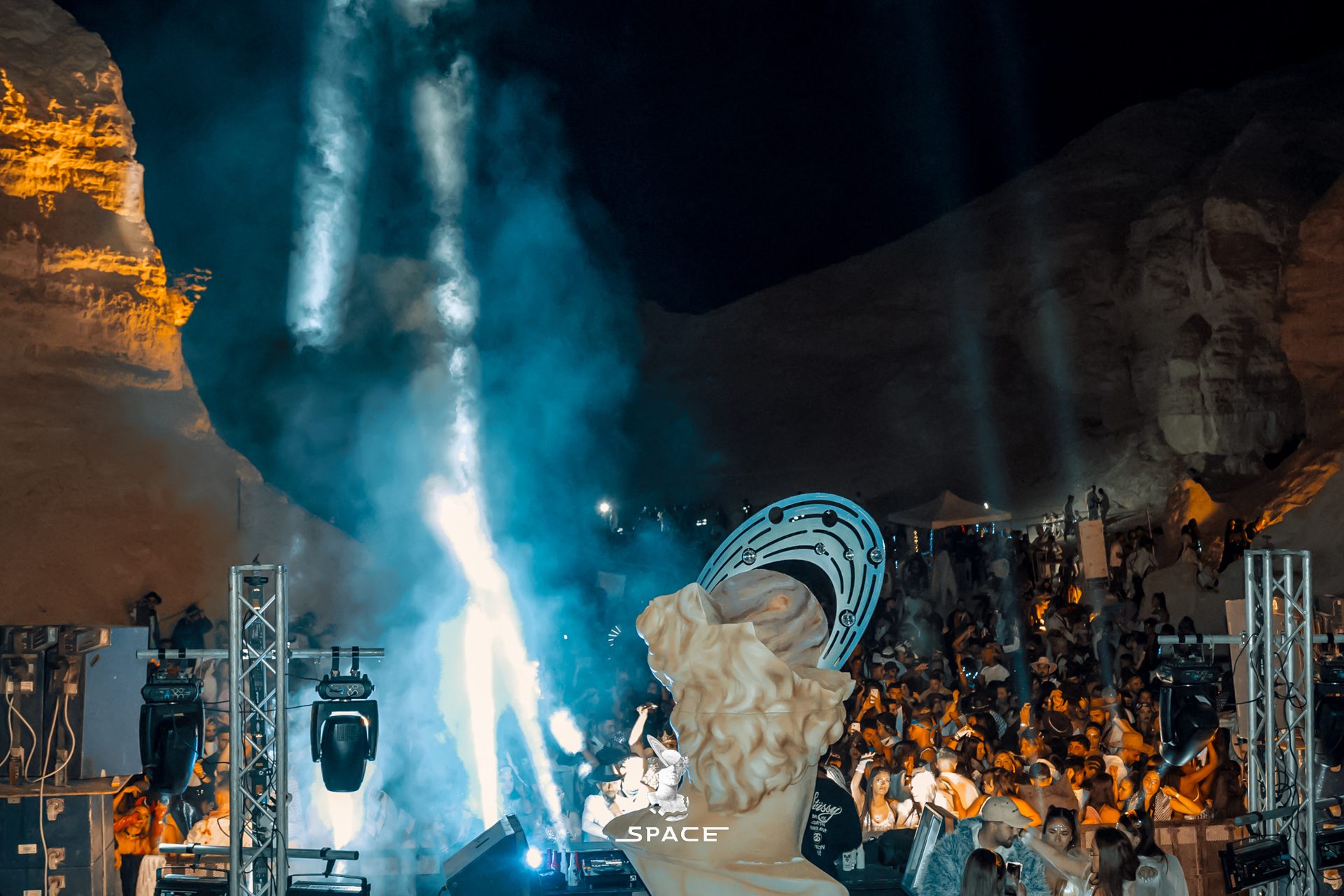 Wide view of a SPACE desert venue at night, stage lights against the rock